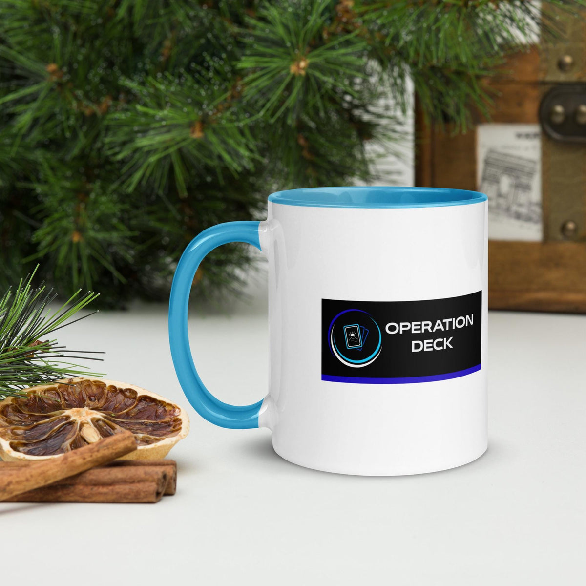 Operation Deck Bien Joué mug logo side with a cyan handle beside holiday greenery.