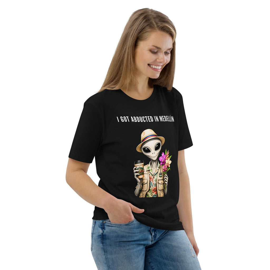 I Got Abducted in Medellin alien T-shirt in black, worn by a smiling model with one hand in a pocket.