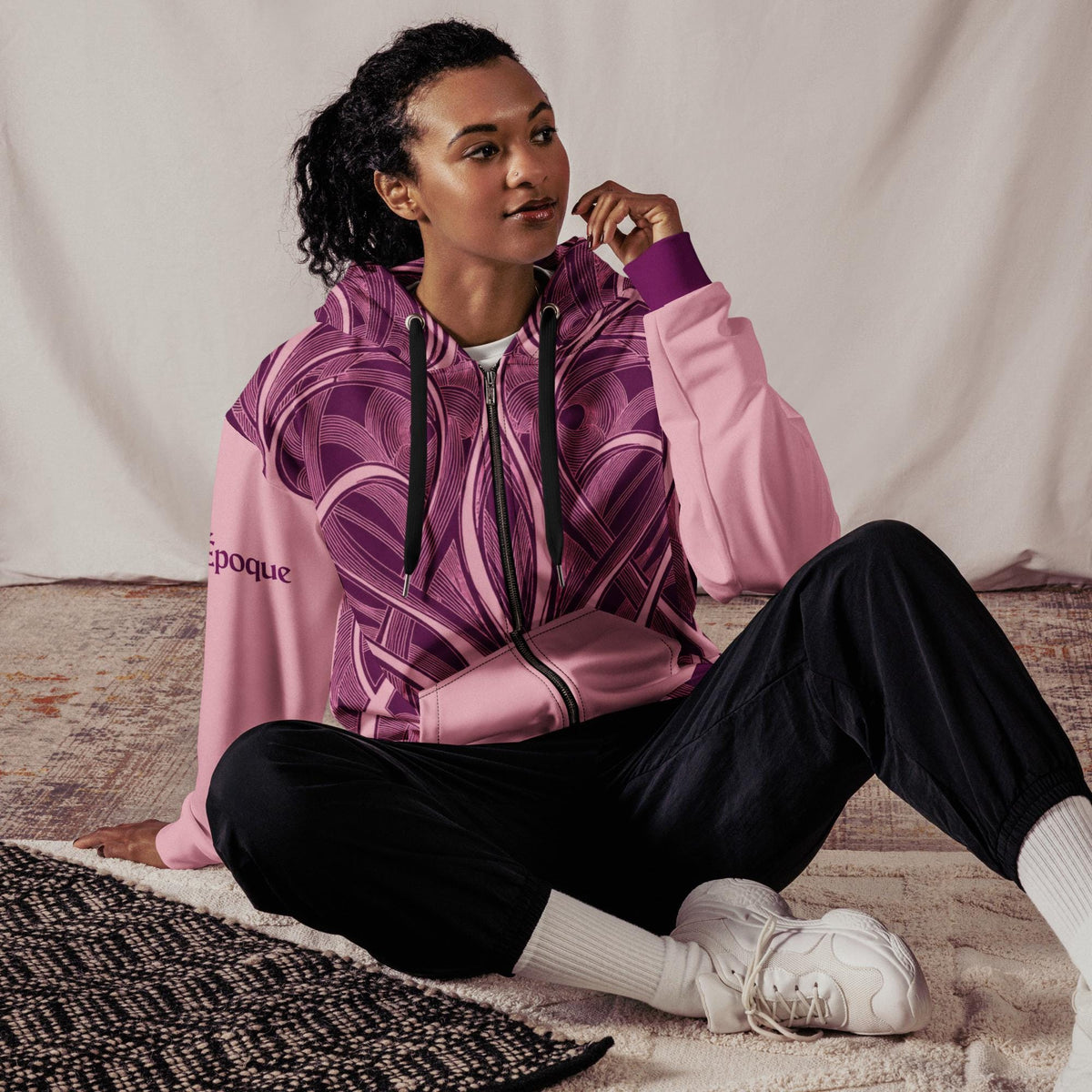 Pink Art Nouveau zip hoodie worn by a seated model indoors.
