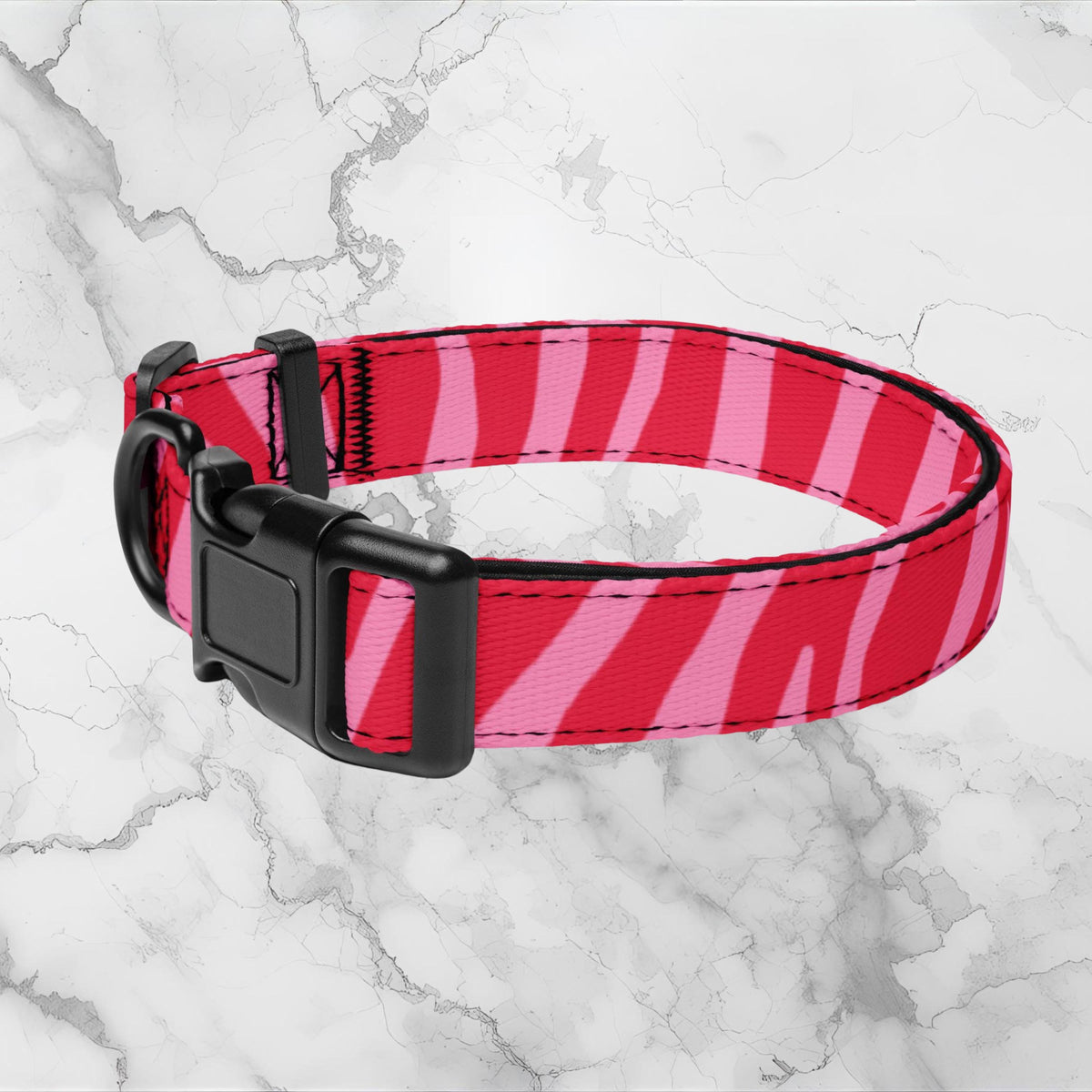 Pink Zebra padded dog collar with pink and red stripes and a black buckle on a pale marble background.