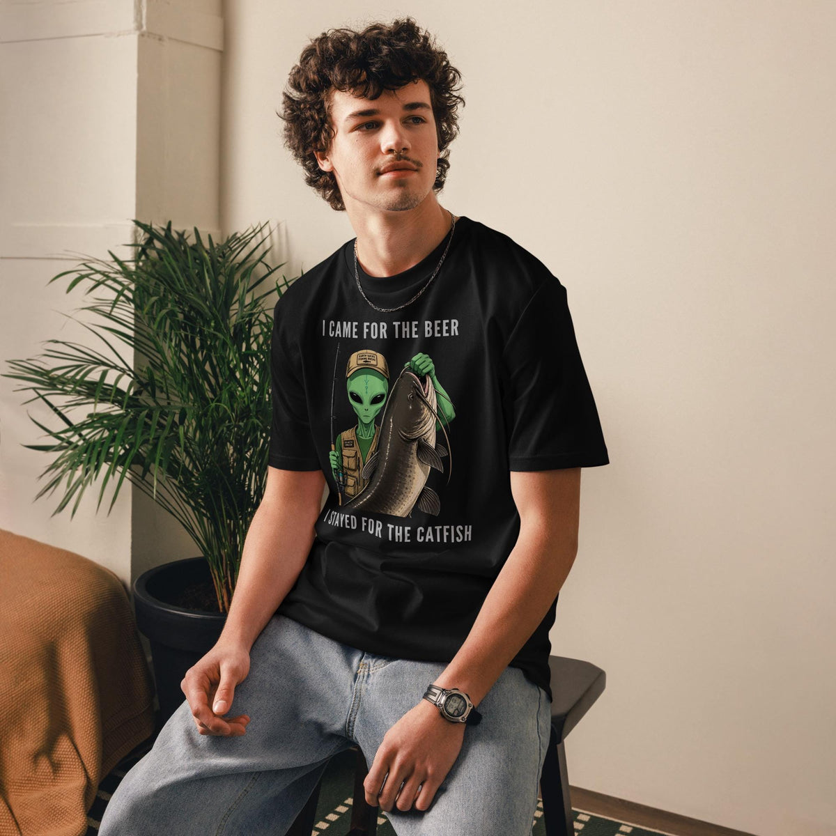 Alien Catfish fishing T-shirt in black, worn by a seated model indoors.