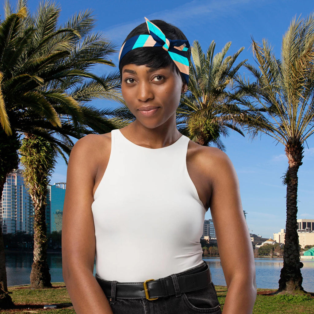Blue Stripe bandana tied as a headband with a bow beside palm trees.