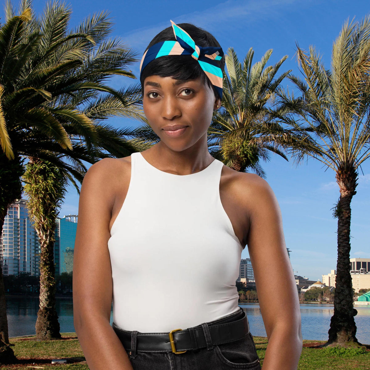 Blue Stripe bandana tied as a headband with a bow beside palm trees.