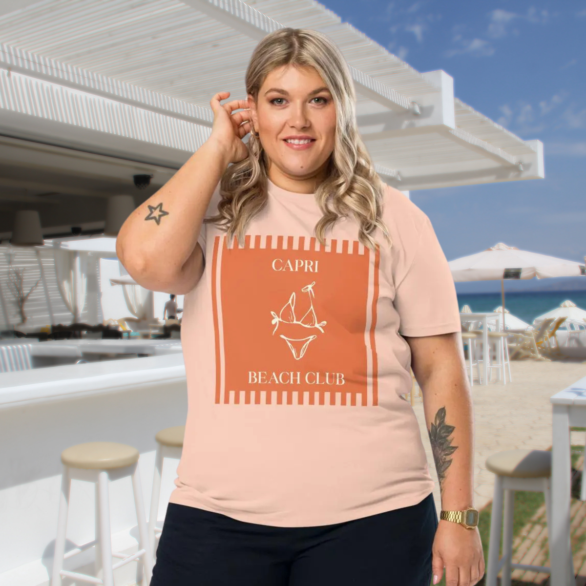 Capri Beach Club T-shirt in peach, worn by a model against a seaside terrace backdrop.