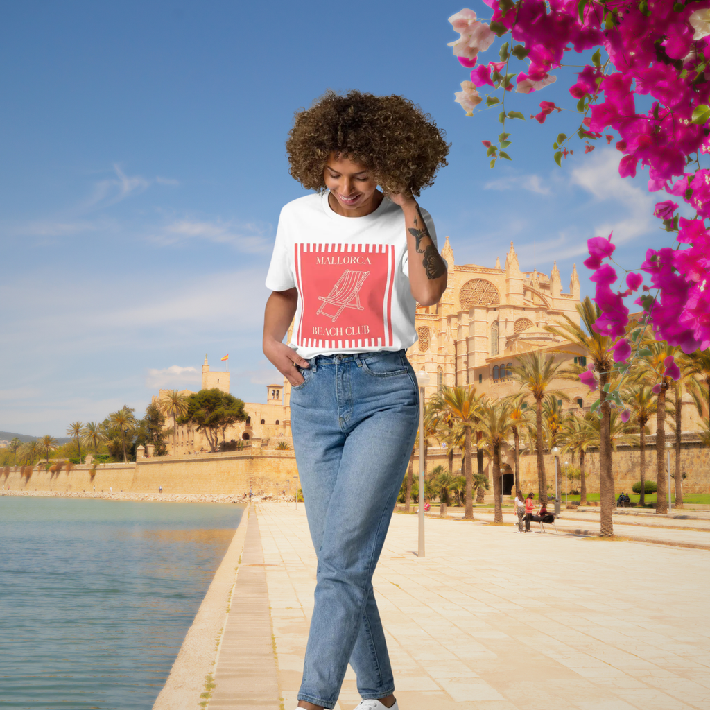 Mallorca Beach Club T-shirt in white, worn by a model on a waterfront promenade.