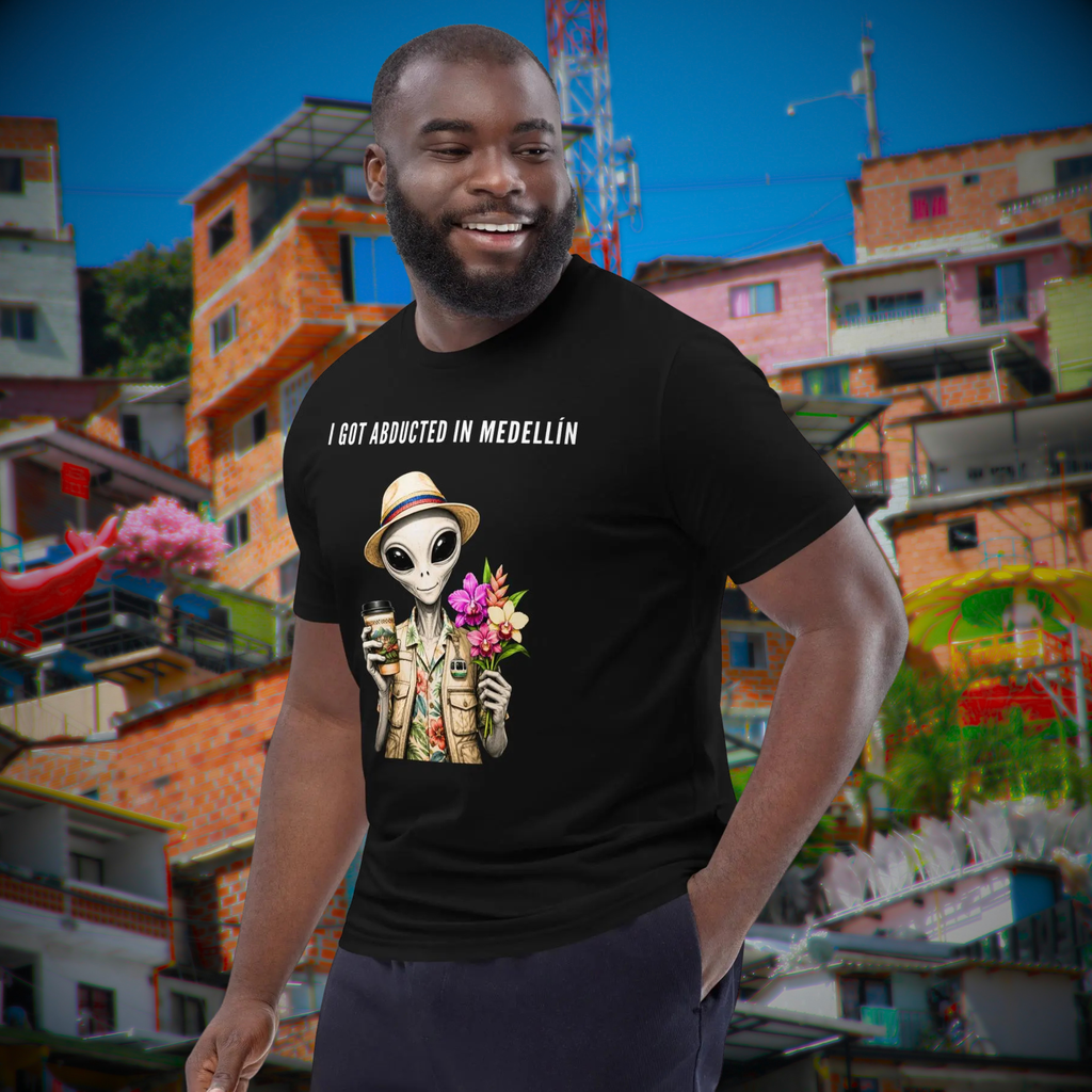 I Got Abducted in Medellin alien T-shirt in black, worn by a smiling model against colorful hillside houses.