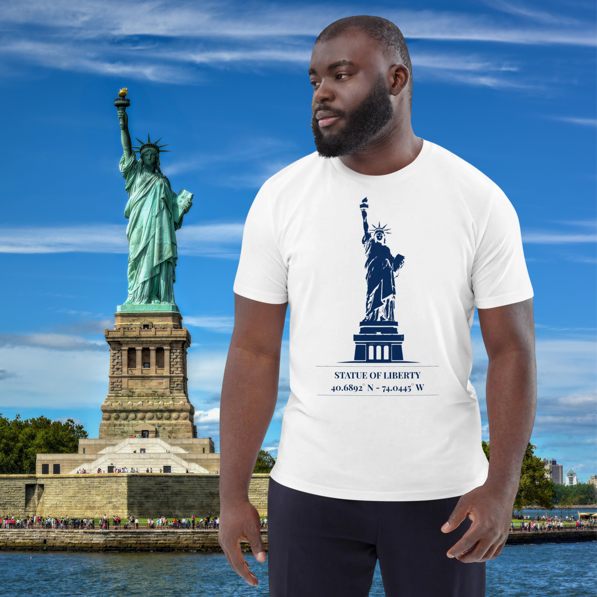 Statue of Liberty coordinates T-shirt in white, worn by a model beside a New York Harbor backdrop.