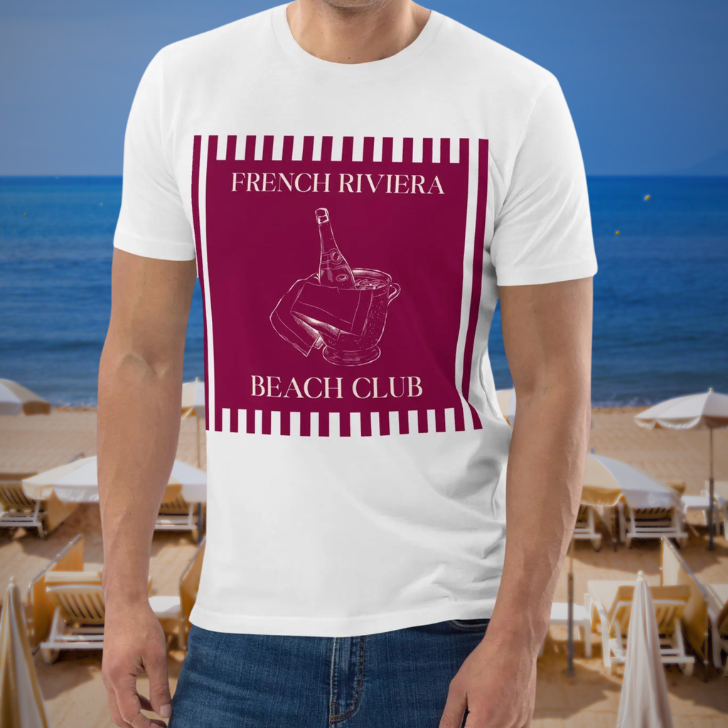 French Riviera Beach Club T-shirt in white, worn by a model beside a seaside restaurant backdrop.