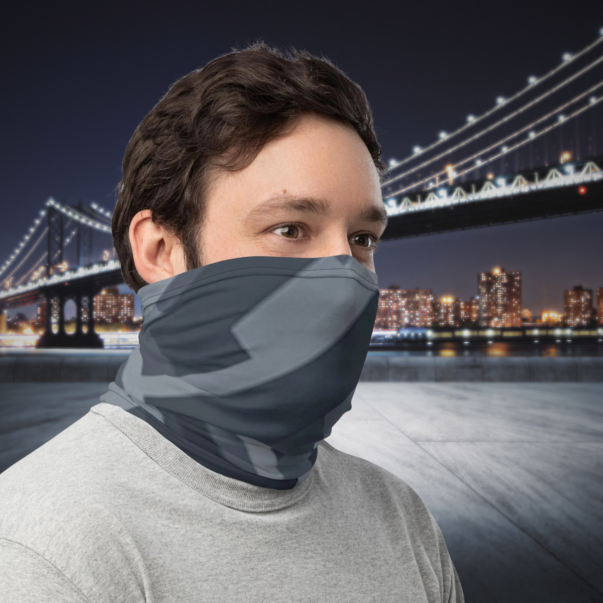 Urban Concrete 8 neck gaiter worn as a face covering beside an illuminated bridge at night.