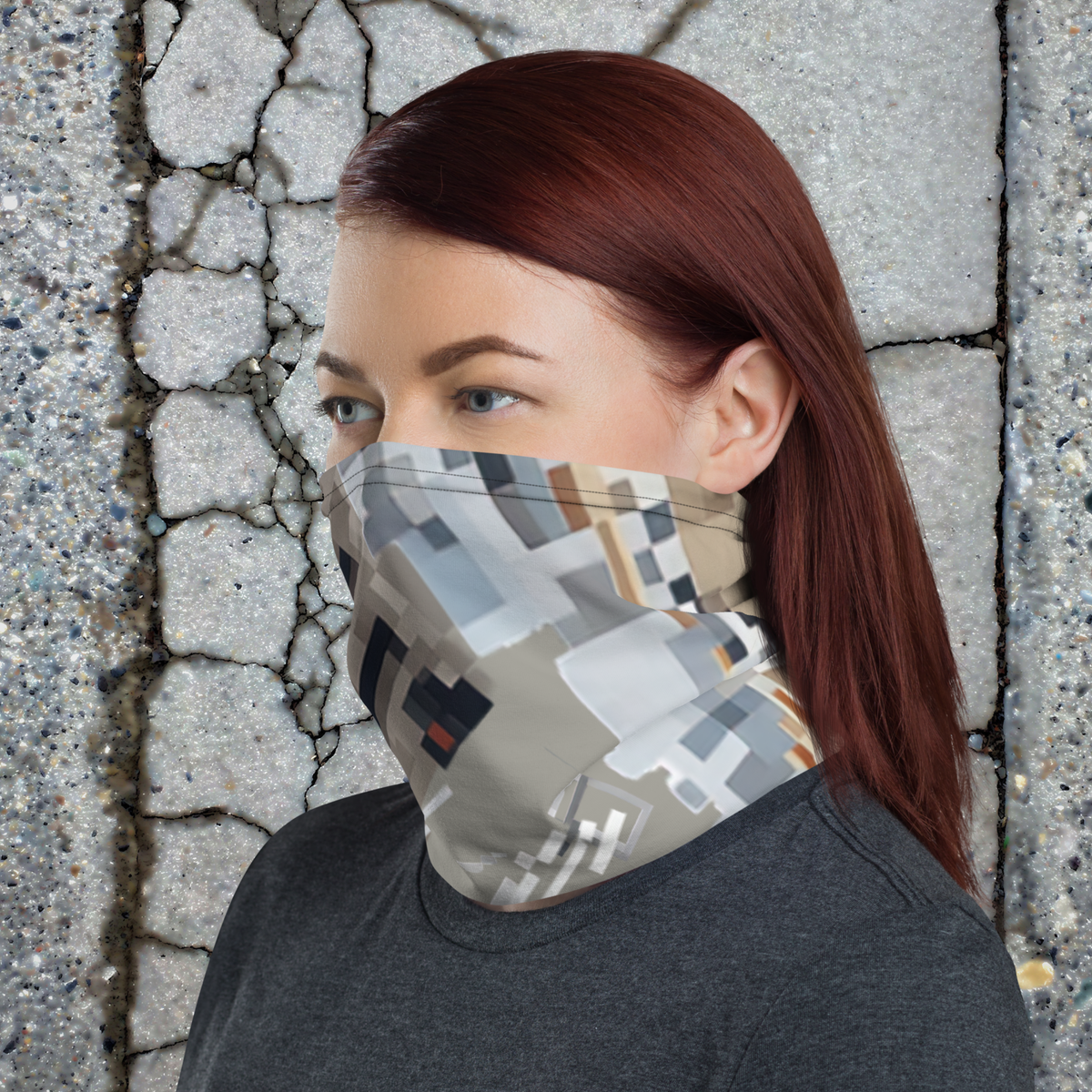 Urban Concrete 10 neck gaiter worn as a face covering beside a stone wall, side view.