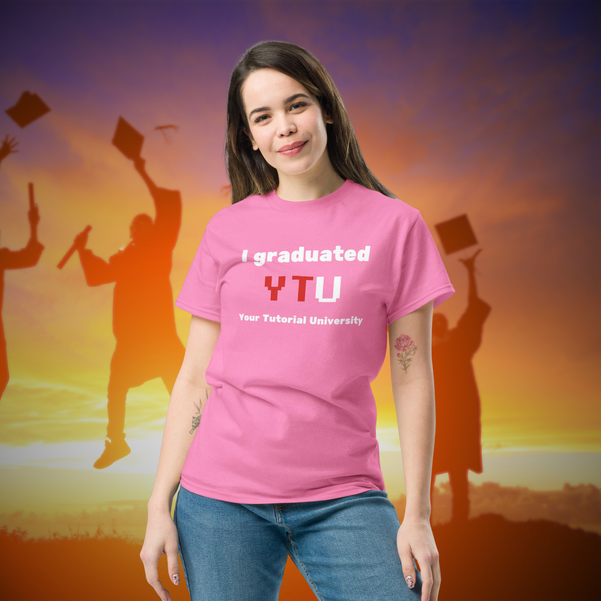 I Graduated YTU T-shirt in pink, worn by a model against a graduation sunset backdrop.