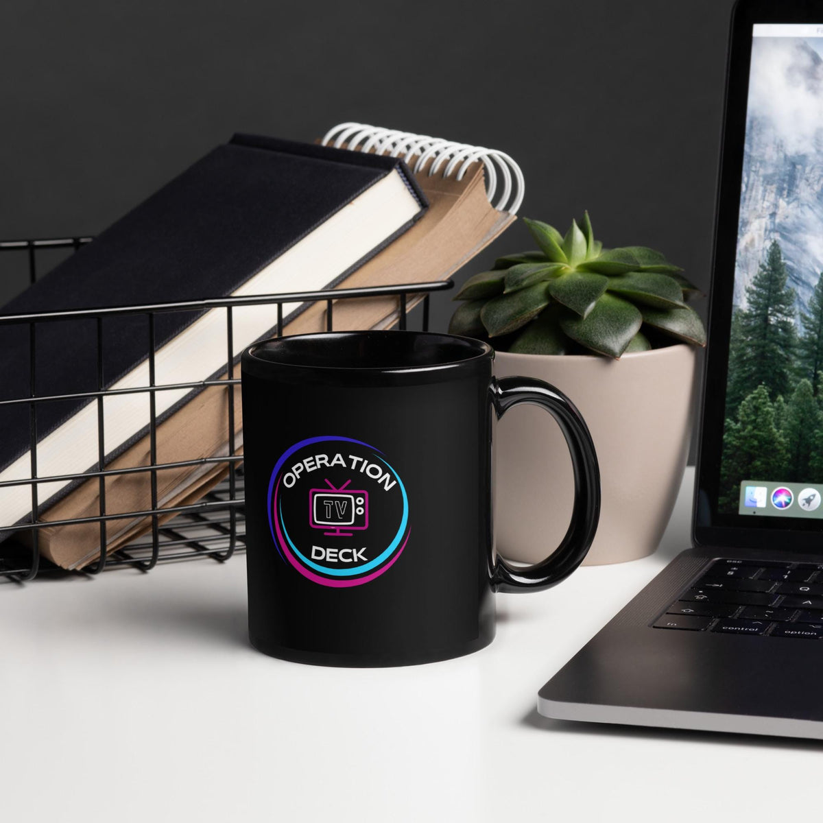 Black Operation Deck gaming mug logo side on a desk beside a laptop and notebooks.