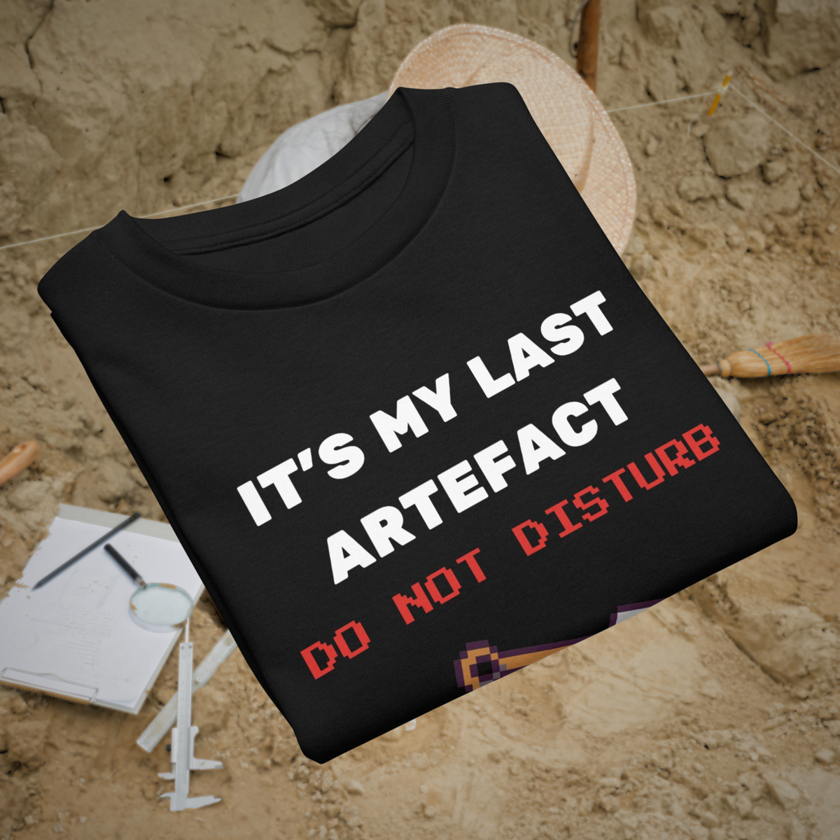 It's My Last Artefact kids' gamer T-shirt in black, folded beside an archaeological hat and notebook.