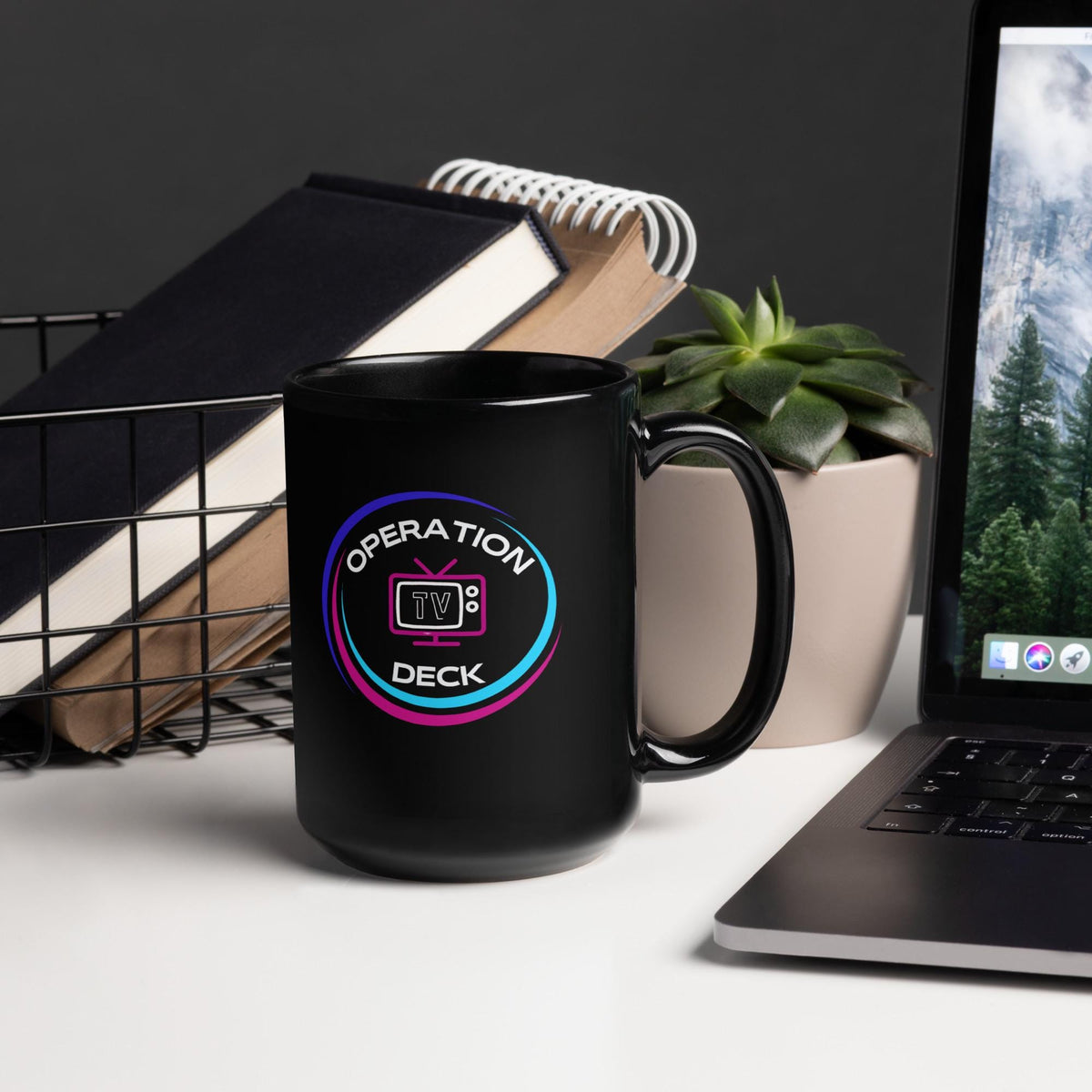 Black Operation Deck gaming mug tall mug logo side beside notebooks and a plant.