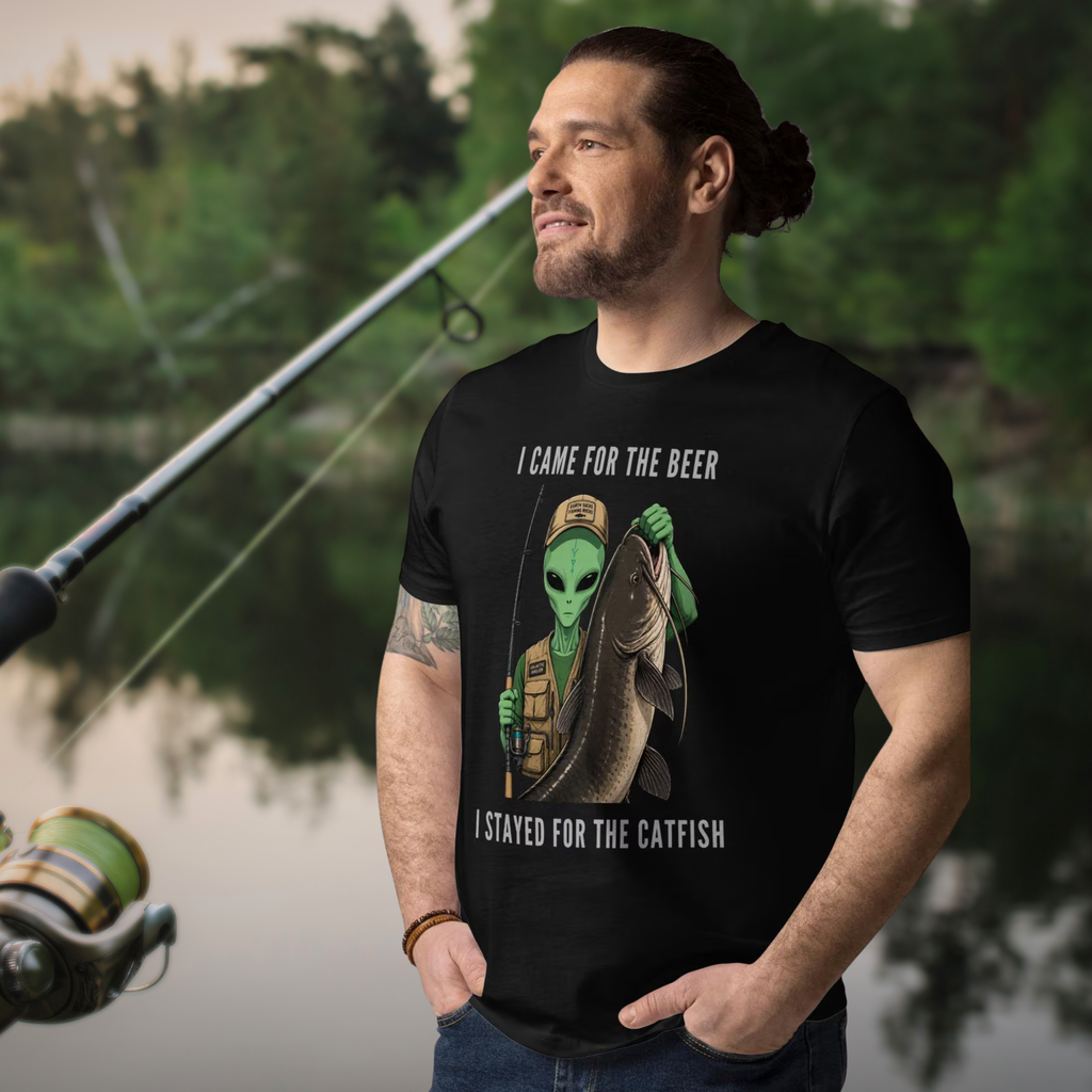 Alien Catfish fishing T-shirt in black, worn by a model beside a fishing rod and water.