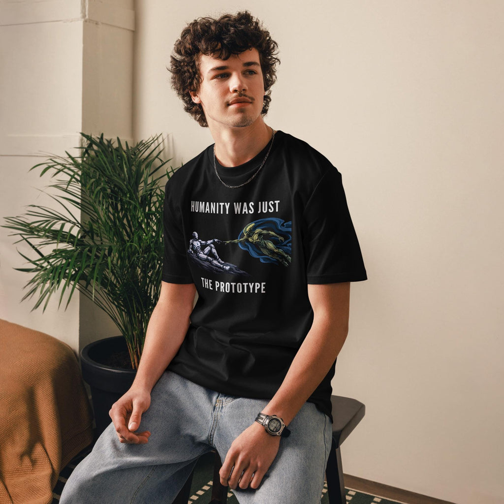 Humanity Prototype AI alien T-shirt in black, worn by a seated model beside indoor plants.