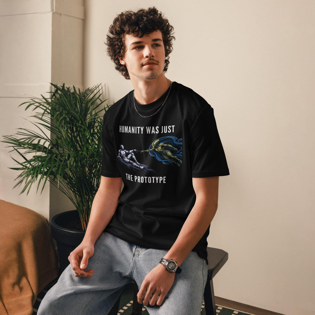 Humanity Prototype AI alien T-shirt in black, worn by a seated model beside indoor plants.