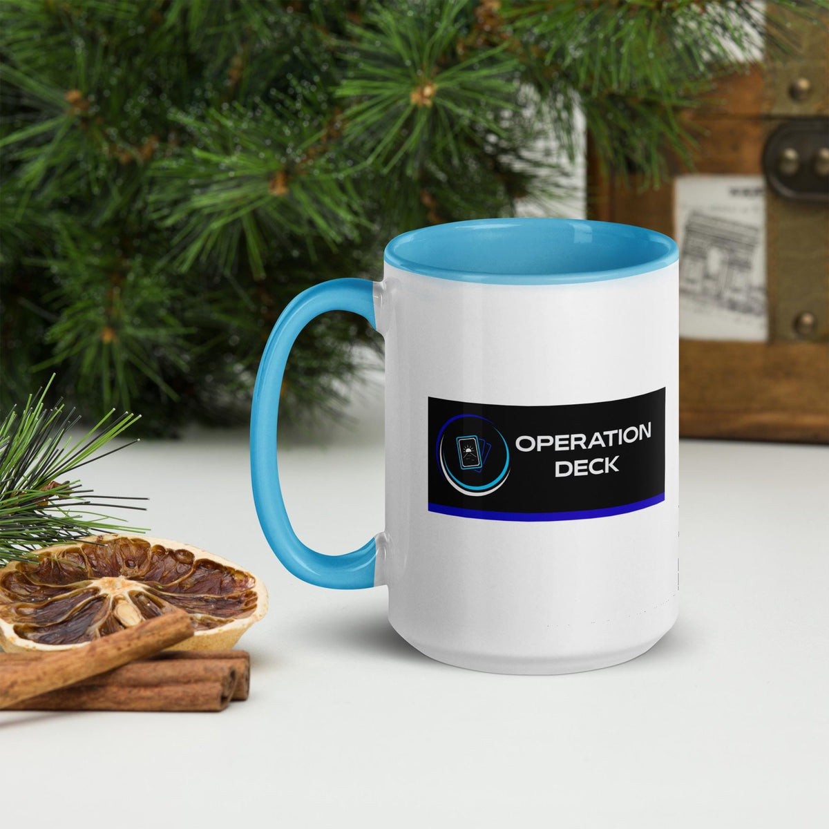 Operation Deck Bien Joué mug logo side beside evergreen branches and dried citrus.