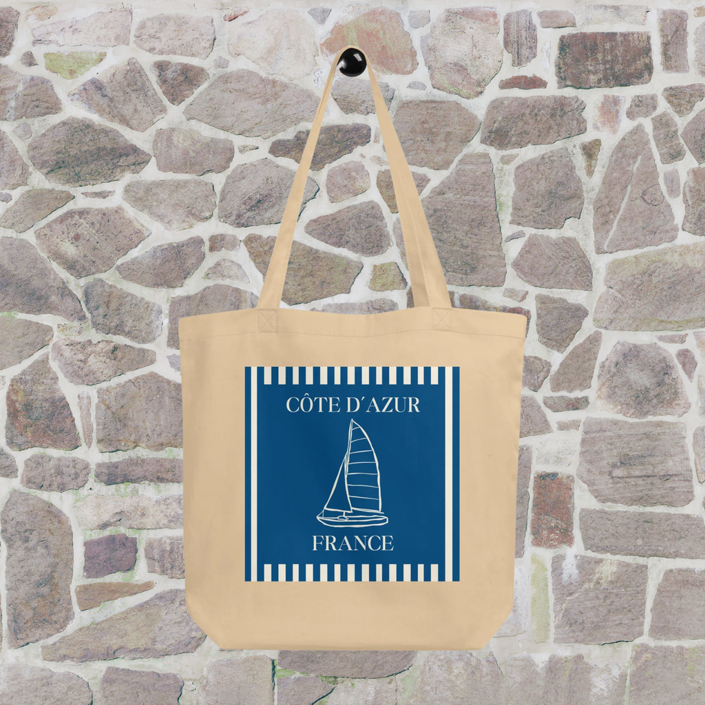 Côte d’Azur sailboat tote hanging against a stone wall, showing the full blue and white graphic.